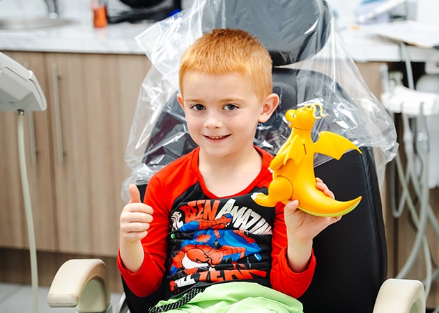 A child at the Fresh Dental Care dental office sitting in the dentist's chair while smiling and holding a toy